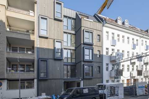 Neubau aus Holz mit modernen Fenstern, Baustelle und Baukran davor.