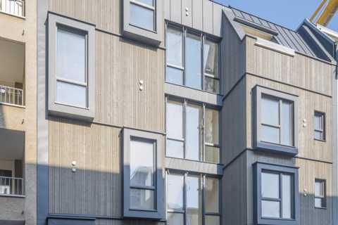 Moderne Wohnhausfassade mit Holzverkleidung und großen rechteckigen Fenstern.