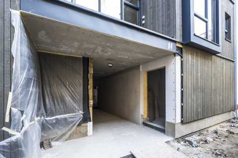 Eingang eines modernen Gebäudes im Bau, mit Holzfassade und überdachtem Durchgang.