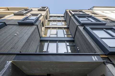 Moderne Hausfassade mit großen Fenstern und der Hausnummer 84, nach oben fotografiert.