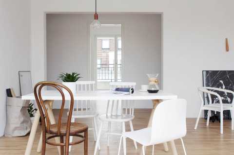 Heller Essbereich mit weißen Stühlen, Holzboden und großem Fenster im Hintergrund.