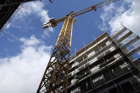 Baukran vor blauem Himmel neben eingerüstetem Gebäude in der Aufsicht.