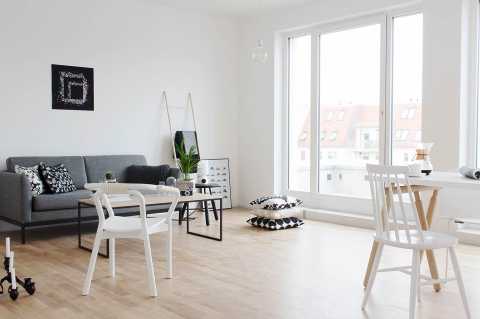 Helles, modernes Wohnzimmer mit grauem Sofa, großen Fenstern und Holzboden.