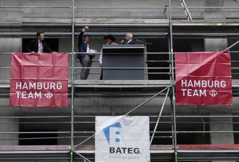 Richtfest auf Baustelle, vier Personen auf Gerüst mit Hamburg Team Bannern.
