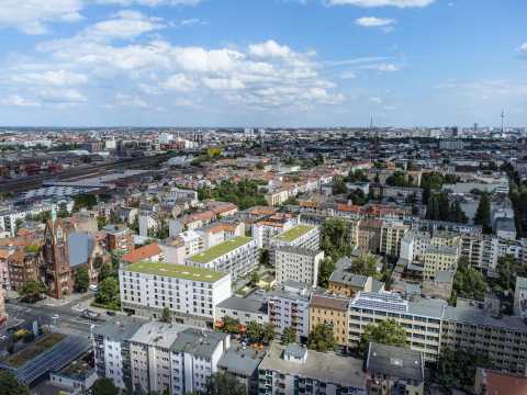 Luftaufnahme einer Stadt mit Wohnhäusern, Kirche, Bahngleisen und blauem Himmel.