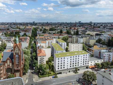 Stadtansicht mit Kirche, modernen Wohnhäusern und begrünten Dächern.