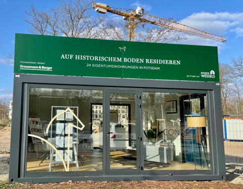 Verkaufscontainer für Eigentumswohnungen, Kran und Bäume im Hintergrund.