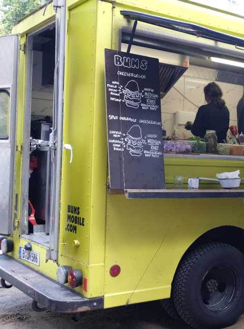 Gelber Foodtruck mit Menütafel für Cheeseburger und Spicy Guacamole Burger.