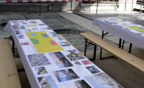 Bierzeltgarnitur mit Fotos und Plänen auf Baustelle, Absperrband im Hintergrund.