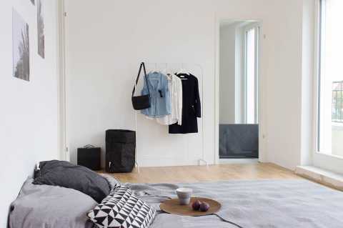 Helles, minimalistisches Schlafzimmer mit Bett, Tablett, Kleiderständer und Fenster.