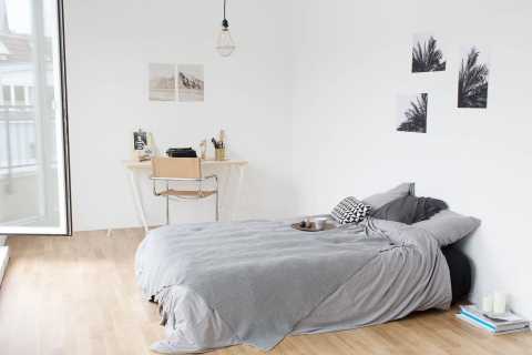 Helles Schlafzimmer mit Bett, Schreibtisch, Wandbildern und Holzboden.