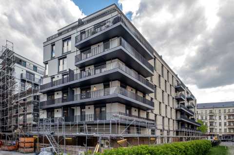 Modernes Wohngebäude mit Balkonen, teils von Gerüsten umgeben, Wolken am Himmel.