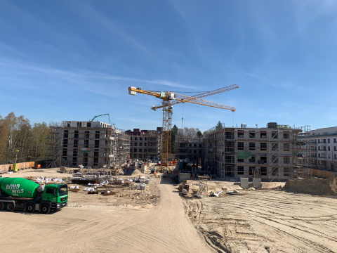 Baustelle mit mehreren Rohbauten, zwei Kränen und einem Betonmischer-Lkw.