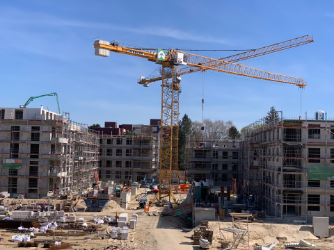 Baustelle mit Baukran, Rohbauten und Baumaterial bei sonnigem Wetter.