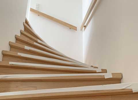 Treppe mit Holzstufen, weißem Klebeband und Holzhandläufen an weißen Wänden.
