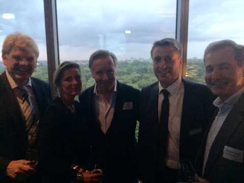 Fünf Personen in Businesskleidung posieren vor Fenster mit Stadtblick.