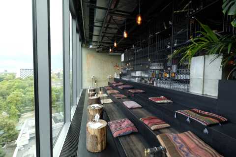 Moderne Lounge mit Kissen auf Treppenstufen, Holztischen und Blick aufs Grüne.