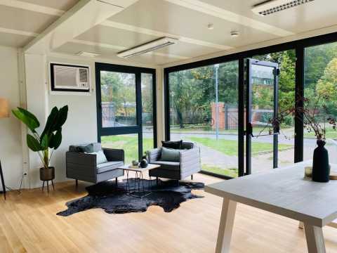 Heller Raum mit großen Fenstern, modernen Sesseln und Pflanzen.