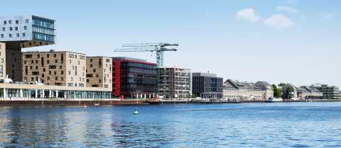Moderne Gebäude und ein Kran am Wasser bei blauem Himmel.