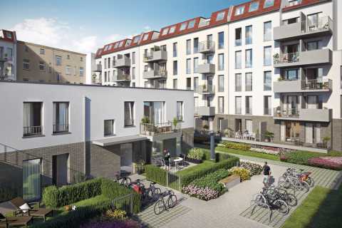 Moderne Wohnanlage mit Gärten, Fahrrädern und Balkonen bei sonnigem Wetter.
