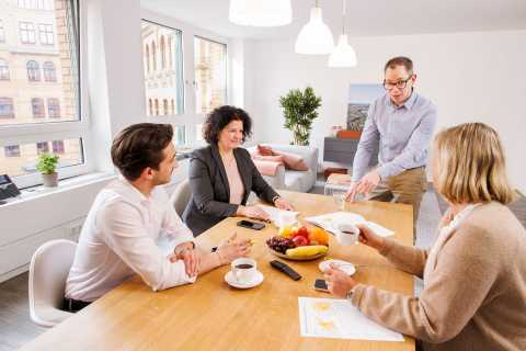 Vier Personen sitzen an einem Tisch im modernen Büro und sprechen miteinander.