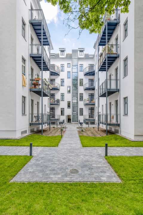 Moderner Innenhof mit Rasen, Wegen und weißen Mehrfamilienhäusern mit Balkonen.