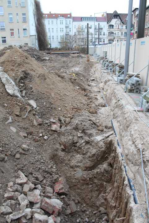 Baustelle mit Erdaushub, Schutt und Baugrube neben Wohnhäusern in der Stadt.