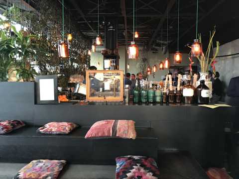 Gemütliche Bar mit bunten Kissen, Pflanzen und warmem Licht.