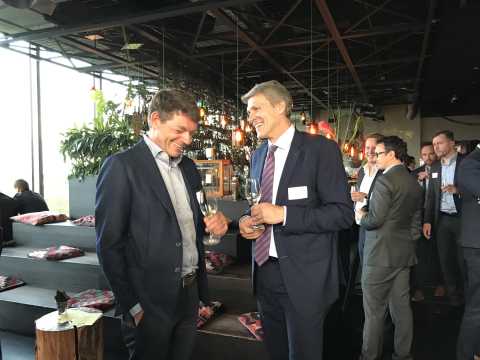 Zwei Männer im Anzug unterhalten sich lachend auf einer Netzwerkveranstaltung.