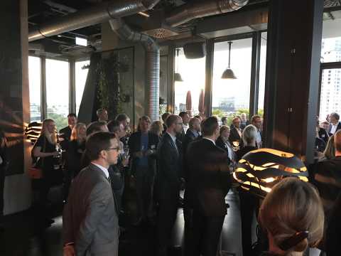 Menschen in formeller Kleidung stehen bei einem Empfang in einem modernen Raum.