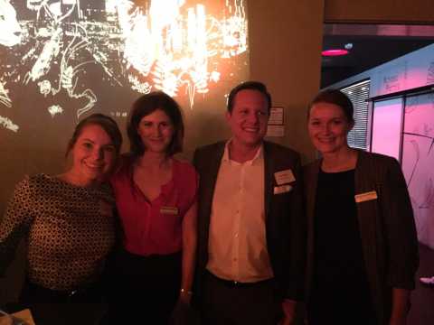 Vier Personen posieren lächelnd vor beleuchteter Wand, Abendveranstaltung.