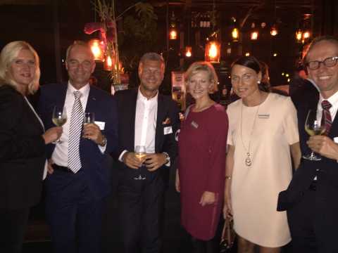 Sechs Personen mit Getränken posieren lächelnd bei einer Abendveranstaltung.