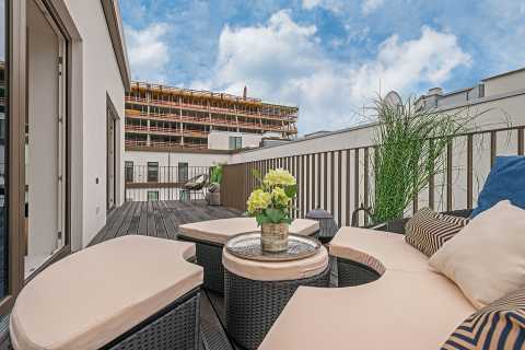 Moderne Dachterrasse mit Sitzmöbeln, Pflanzen und Blick auf Neubau.