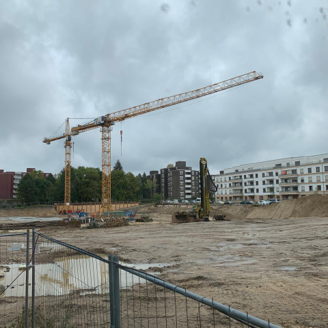 Baustelle mit zwei Kränen, Baugrube, Bagger und Wohngebäuden im Hintergrund.