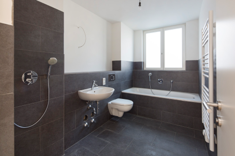 Modernes, leeres Badezimmer mit dunklen Fliesen, Badewanne und Fenster.