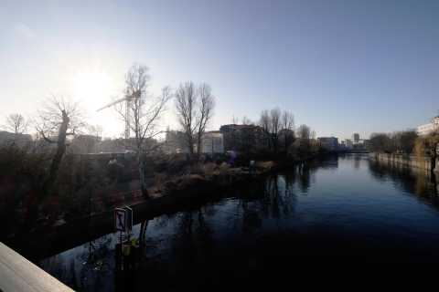 Sonnenaufgang über einem Fluss mit kahlen Bäumen und Stadt im Hintergrund.