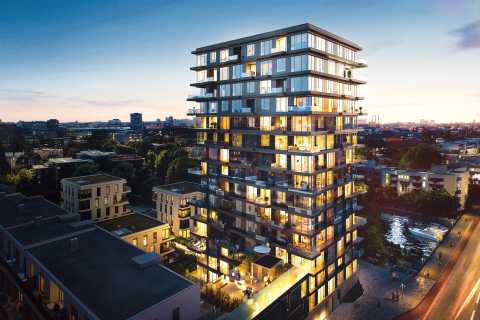 Modernes Hochhaus bei Sonnenuntergang, beleuchtete Fenster, Stadt im Hintergrund.