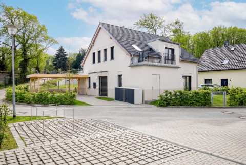 Modernes Einfamilienhaus mit Balkon, Carport und Garten an einer ruhigen Straße.