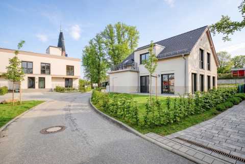 Moderne Wohnhäuser mit Vorgarten, gepflastertem Weg und grüner Bepflanzung.