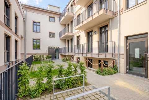 Moderner Innenhof eines Wohnhauses mit Balkonen, Pflanzen und großen Fenstern.