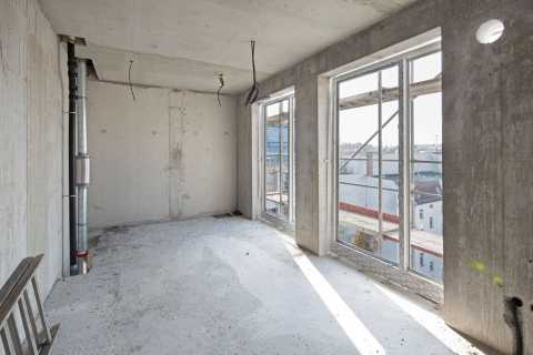 Rohbauzimmer mit großen Fenstern und Blick auf Gerüst und Stadt.