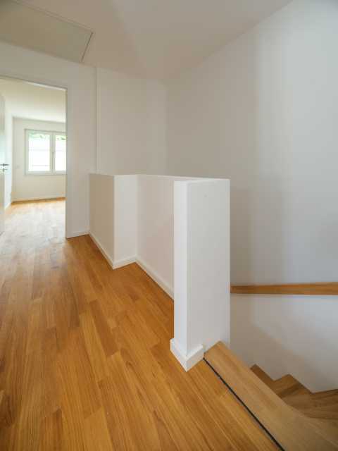 Helles Treppenhaus mit Holzfußboden und Blick in ein Zimmer mit Fenster.