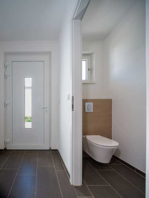 Eingangsbereich mit Blick in ein kleines, modernes WC mit Wandtoilette.