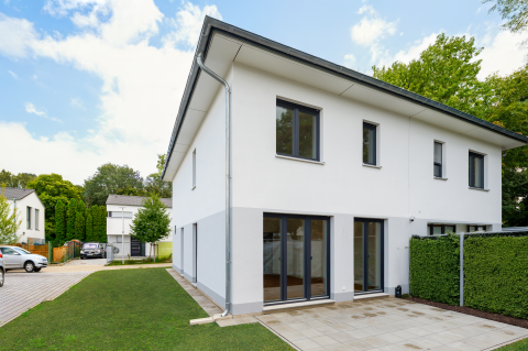 Modernes weißes Zweifamilienhaus mit Terrasse, Garten und großen Fenstern.
