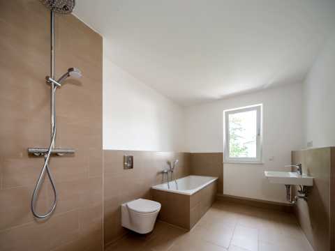 Modernes Bad mit beiger Fliesen, Dusche, WC, Badewanne, Fenster und Waschbecken.