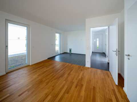 Leeres, helles Zimmer mit Parkettboden, offenen Türen und großen Fenstern.