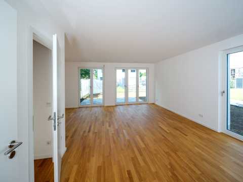 Helles, leeres Zimmer mit Parkettboden und großen Fensterfronten zur Terrasse.