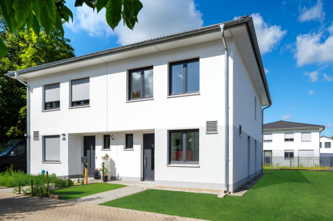 Modernes weißes Doppelhaus mit Garten vor blauem Himmel und Nachbarhaus.
