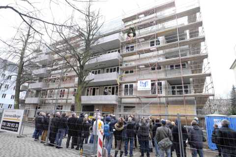 Menschenmenge vor im Bau befindlichem Wohnhaus mit Gerüst und Richtkranz.