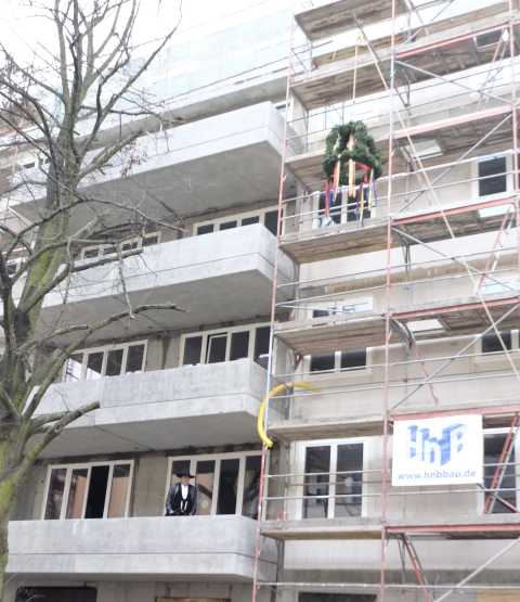 Richtfest an Neubau mit Baum, Gerüst, Richtkranz und Zimmermann auf Balkon.